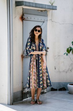 uzun boylu, zarif ve güzel Hint Asyalı kadın yaz elbise ve güneş gözlüğü gülümsüyor o pozlar gün boyunca bir arka sokakta bir sokakta olarak içinde