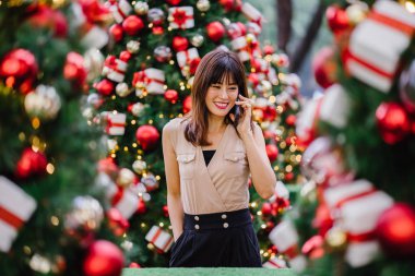 güzel orta yaşlı kadın mutlu onun smartphone üzerinde konuşuyor ve aynı derecede o durgunluk ortasında güzel gülümseyen gün boyunca Noel ağaçları dekore edilmiş olan