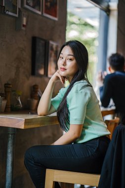 Genç ve çekici Çinli Asyalı bir kadının portresi uzanarak ve bir hafta sonu gün boyunca bir kafede rahatlatıcı. Nane yeşili bir kazak giyiyor.