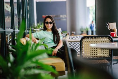 Genç ve çekici Çinli Asyalı bir kadının portresi uzanarak ve bir hafta sonu gün boyunca bir kafede rahatlatıcı. Nane yeşili bir kazak giyiyor.