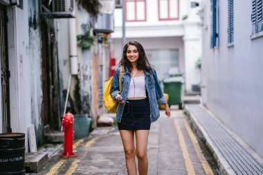 Bir genç ve çekici Hint Asyalı kadın bir kot ceket ve sarı sırt çantası onun kulaklıklar üzerinde müzik keyfi portresi