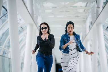 İki farklı arkadaş, iyi aydınlatılmış beyaz fütüristik bir üstgeçit köprüsünden kameraya doğru koşuyorlar. Biri Müslüman bir Orta Doğulu kadın, diğeri de Çinli..