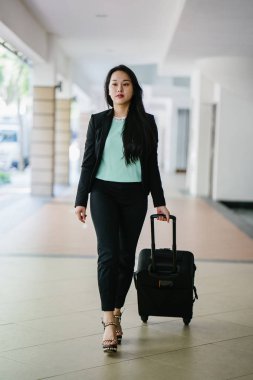 Genç bir Asyalı kadın bavulunu çekiyor. O çekici, zarif ve şık giyinmiş