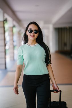 Genç bir Asyalı kadın bavulunu çekiyor. O çekici, zarif ve şık giyinmiş