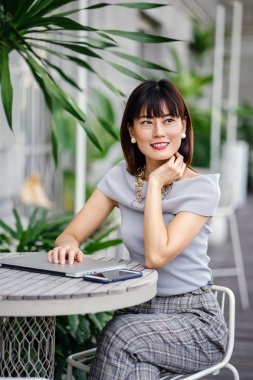 Açık havada şık bir yerde oturan bir emin, şık ve çekici orta yaşlı Çinli Asyalı kadın portresi. O bir pohpohlama gri kıyafeti giyiyor.