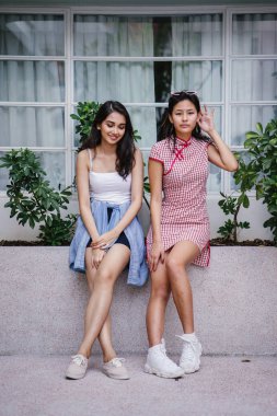 farklı etnik yapı birlikte dışarı asılı iki genç kadın arkadaşlar. Bir Çinli bir kadını bir cheongsam ve diğer bir Hint kadının modaya uygun bir kıyafet olduğunu