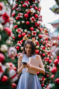 Genç, güzel ve mutlu bir Hint Asyalı kadın şenlikli Noel portresi bir hediye bir Noel ağacı önünde tutan gülümseyerek.