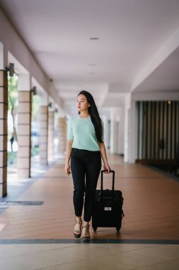 Genç bir Asyalı kadın bavulunu çekiyor. O çekici, zarif ve şık giyinmiş