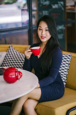 Bir açık havada açık havada oturan ve kırmızı bir çay seti çay sıcak bir fincan zevk genç, çekici, zarif ve güzel Asyalı kadın Portresi. 