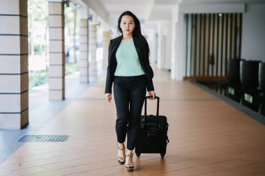 Genç bir Asyalı kadın bavulunu çekiyor. O çekici, zarif ve şık giyinmiş