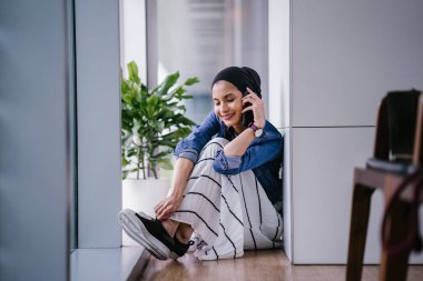 Genç bir Ortadoğulu Müslüman kadın gün boyunca bir ofiste, ortak çalışma alanında veya kütüphanede oturuyor ve akıllı telefonunu kullanıyor. Başörtüsü takıyor (başörtüsü)).