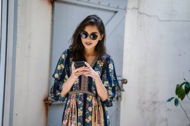Bir elbise ve onun smartphone ile güneş gözlüğü takan bir genç, çekici ve güzel Hint Asyalı kadın portresi