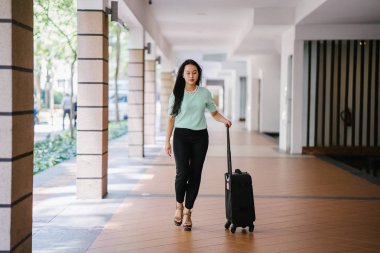 Genç bir Asyalı kadın bavulunu çekiyor. O çekici, zarif ve şık giyinmiş