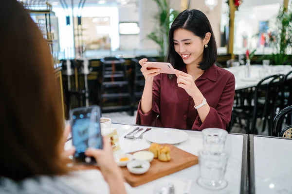 Şık bir kapalı kafede oturan ve akıllı telefon tutan güzel ve zarif genç Koreli Asyalı kadının bir portre