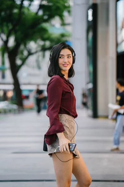 beautiful Korean woman in an elegant blouse and shorts dancing as she walks down a street in the city with her headphones on