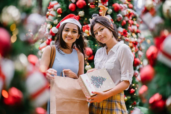 İki genç Asyalı kızlar exchange bir başka gün boyunca şehrin bir sokakta bir şekilde dekore edilmiş bir Noel ağacı altında sunuyor. Hint, diğer Çinli biri