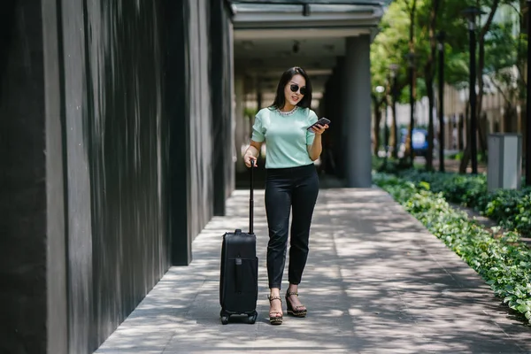 O bir yolculuk dolu uygulama üzerinden rezervasyonu onu binmek için caddenin kenarında bekleyen zarif ve güzel bir genç Asyalı kadının portresi. Tekerlekli bir bavula tutunuyor.. 