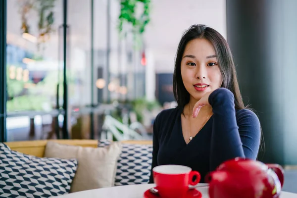 Bir açık havada açık havada oturan ve kırmızı bir çay seti çay sıcak bir fincan zevk genç, çekici, zarif ve güzel Asyalı kadın Portresi. 