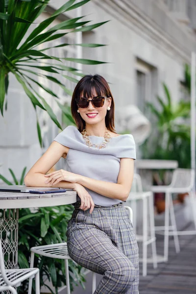 Açık havada şık bir yerde oturan bir emin, şık ve çekici orta yaşlı Çinli Asyalı kadın portresi. O bir pohpohlama gri kıyafeti giyiyor.