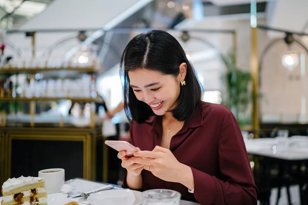 Şık bir kapalı kafede oturan ve akıllı telefon tutan güzel ve zarif genç Koreli Asyalı kadının bir portre