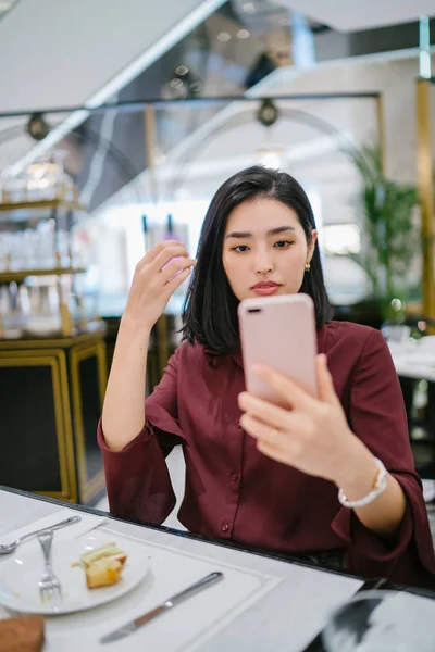 Şık bir kapalı kafede oturan ve akıllı telefon tutan güzel ve zarif genç Koreli Asyalı kadının bir portre