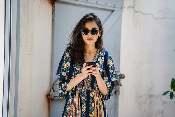 Bir elbise ve onun smartphone ile güneş gözlüğü takan bir genç, çekici ve güzel Hint Asyalı kadın portresi