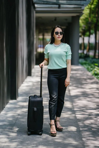 Genç bir Asyalı kadın bavulunu çekiyor. O çekici, zarif ve şık giyinmiş