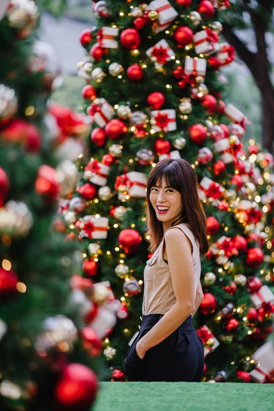 中国アジア観光女性笑顔と市内で日中に美しく飾られたクリスマス ツリーを持つ肖像画のためにポーズ — ストック写真