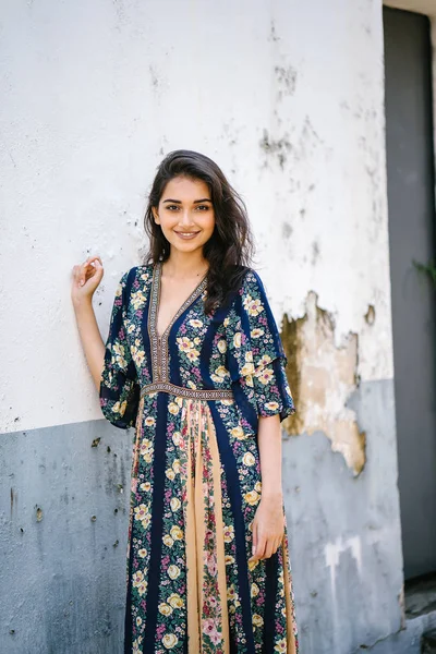 portrait of a tall, young, elegant and beautiful Indian Asian woman in flowing dress against a weathered wall on a street