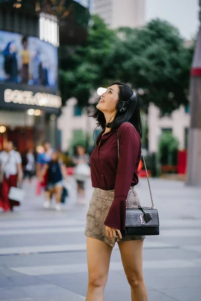 beautiful Korean woman in an elegant blouse and shorts dancing as she walks down a street in the city with her headphones on