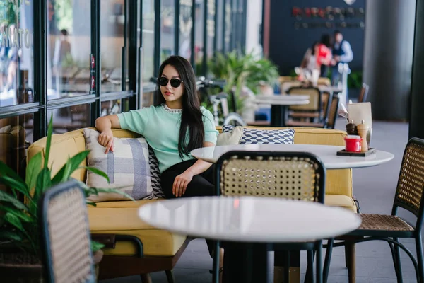 Genç ve çekici Çinli Asyalı bir kadının portresi uzanarak ve bir hafta sonu gün boyunca bir kafede rahatlatıcı. Nane yeşili bir kazak giyiyor.