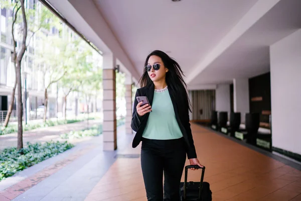 O bir yolculuk dolu uygulama üzerinden rezervasyonu onu binmek için caddenin kenarında bekleyen zarif ve güzel bir genç Asyalı kadının portresi. Tekerlekli bir bavula tutunuyor.. 
