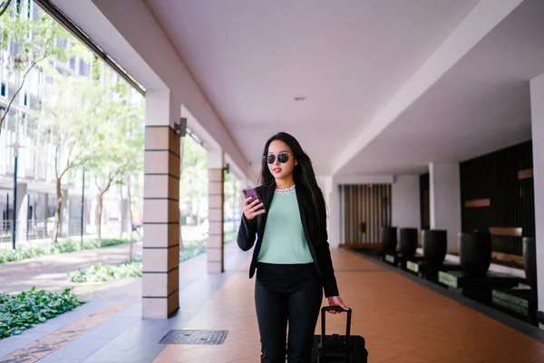 O bir yolculuk dolu uygulama üzerinden rezervasyonu onu binmek için caddenin kenarında bekleyen zarif ve güzel bir genç Asyalı kadının portresi. Tekerlekli bir bavula tutunuyor.. 