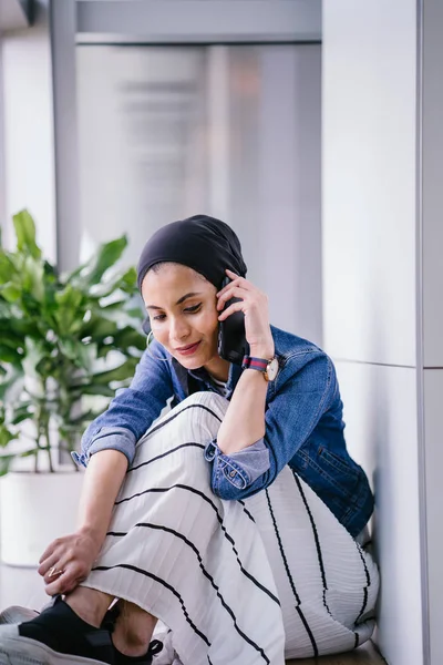 Genç bir Ortadoğulu Müslüman kadın gün boyunca bir ofiste, ortak çalışma alanında veya kütüphanede oturuyor ve akıllı telefonunu kullanıyor. Başörtüsü takıyor (başörtüsü)).