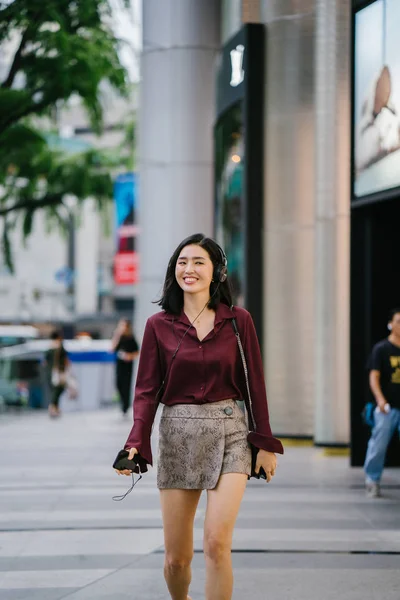 美丽的韩国女人穿着一件优雅的衬衫和短裤跳舞 她走在城市的街道上 戴着耳机 — 图库照片