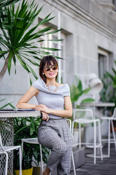 Açık havada şık bir yerde oturan bir emin, şık ve çekici orta yaşlı Çinli Asyalı kadın portresi. O bir pohpohlama gri kıyafeti giyiyor.