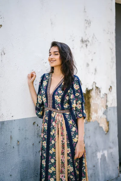 portrait of a tall, young, elegant and beautiful Indian Asian woman in flowing dress against a weathered wall on a street