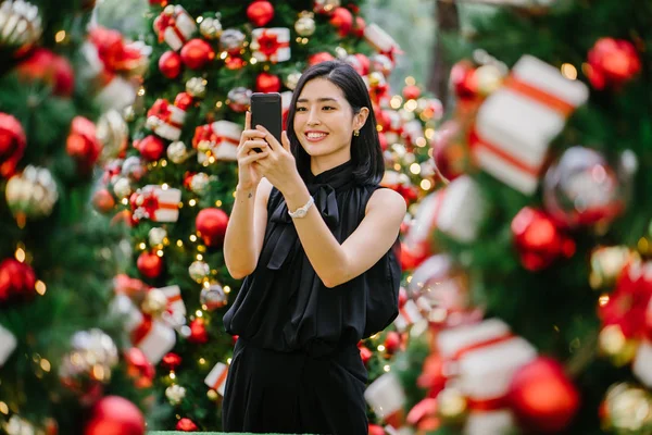 beautiful Korean woman smiles as she takes photographs of decorated Christmas trees