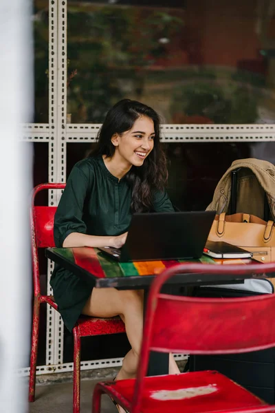 young university student (Indian Asian woman) is studying and working on her laptop computer at a table during the day