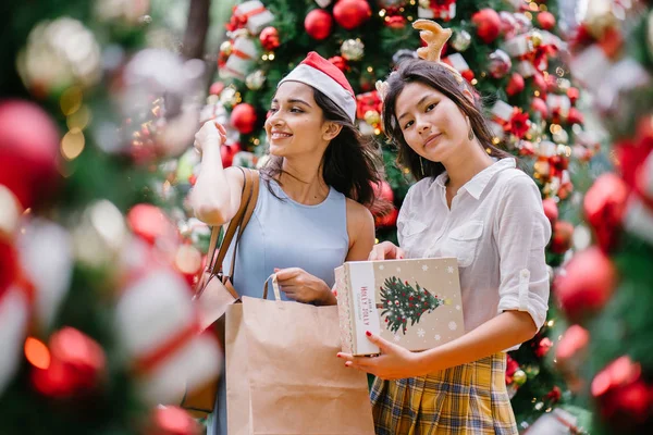 İki genç Asyalı kızlar exchange bir başka gün boyunca şehrin bir sokakta bir şekilde dekore edilmiş bir Noel ağacı altında sunuyor. Hint, diğer Çinli biri