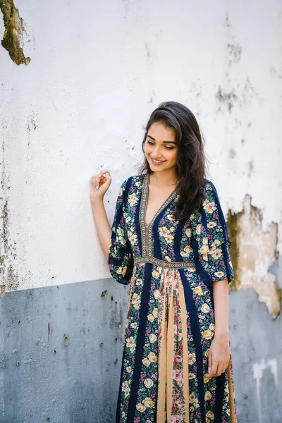 bir sokakta yıpranmış bir duvara portre genç bir uzun boylu, zarif ve güzel Hint Asyalı kadın akan içinde elbise 
