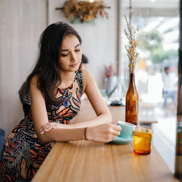 年轻美丽的印度亚裔新加坡妇女穿着印花礼服坐在咖啡馆里 享受周末在亚洲 — 图库照片