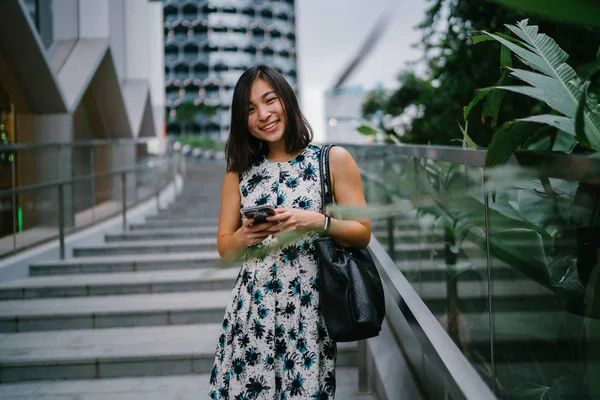 中国のアジア人女性が日中 シンガポール アジアの都市 の石段に座りながら スマートフォンを使ってテキストメッセージを送っている 彼女は若く 魅力的で 生命に満ちている — ストック写真