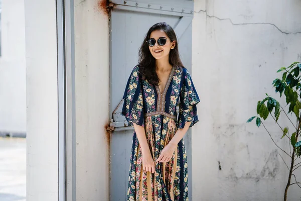 uzun boylu, zarif ve güzel Hint Asyalı kadın yaz elbise ve güneş gözlüğü gülümsüyor o pozlar gün boyunca bir arka sokakta bir sokakta olarak içinde