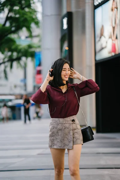 エレガントなブラウスとショート パンツに彼女彼女のヘッドフォンが付いている都市の通りを歩くとダンスで美しい韓国女性 — ストック写真
