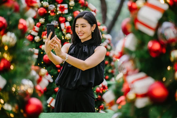 beautiful Korean woman smiles as she takes photographs of decorated Christmas trees