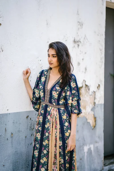 bir sokakta yıpranmış bir duvara portre genç bir uzun boylu, zarif ve güzel Hint Asyalı kadın akan içinde elbise 