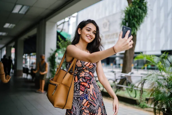 Genç, güzel ve zarif Punjabi Hint Asyalı kadın kendini bir selfie onun smartphone ile yoğun bir cadde üzerinde gün boyunca alır