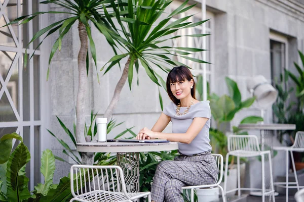 Açık havada şık bir yerde oturan bir emin, şık ve çekici orta yaşlı Çinli Asyalı kadın portresi. O bir pohpohlama gri kıyafeti giyiyor.