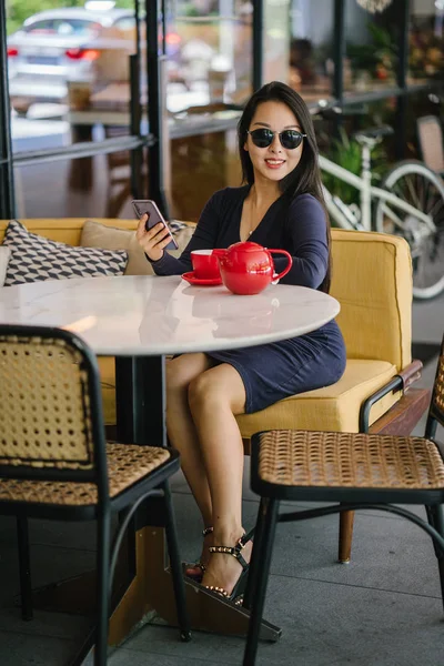 Bir açık havada açık havada oturan ve kırmızı bir çay seti çay sıcak bir fincan zevk genç, çekici, zarif ve güzel Asyalı kadın Portresi. 